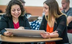 two women sitting at table looking at poster